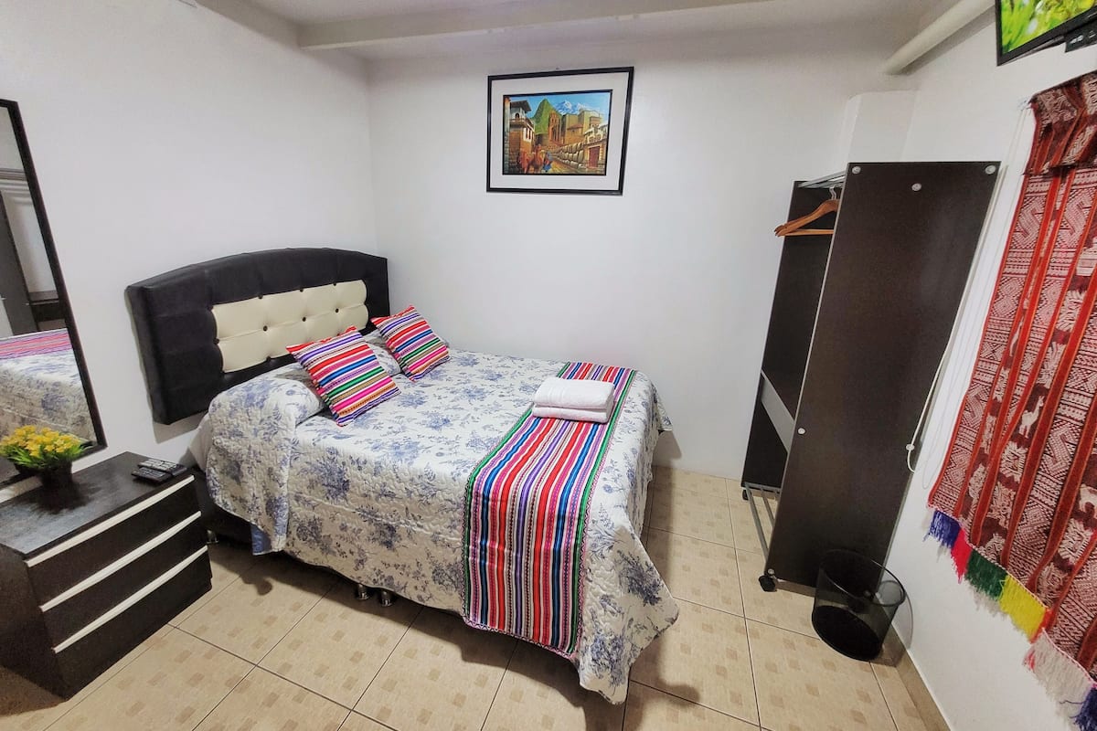 A bedroom with a bed, a dresser, a mirror, a painting, and a wardrobe.