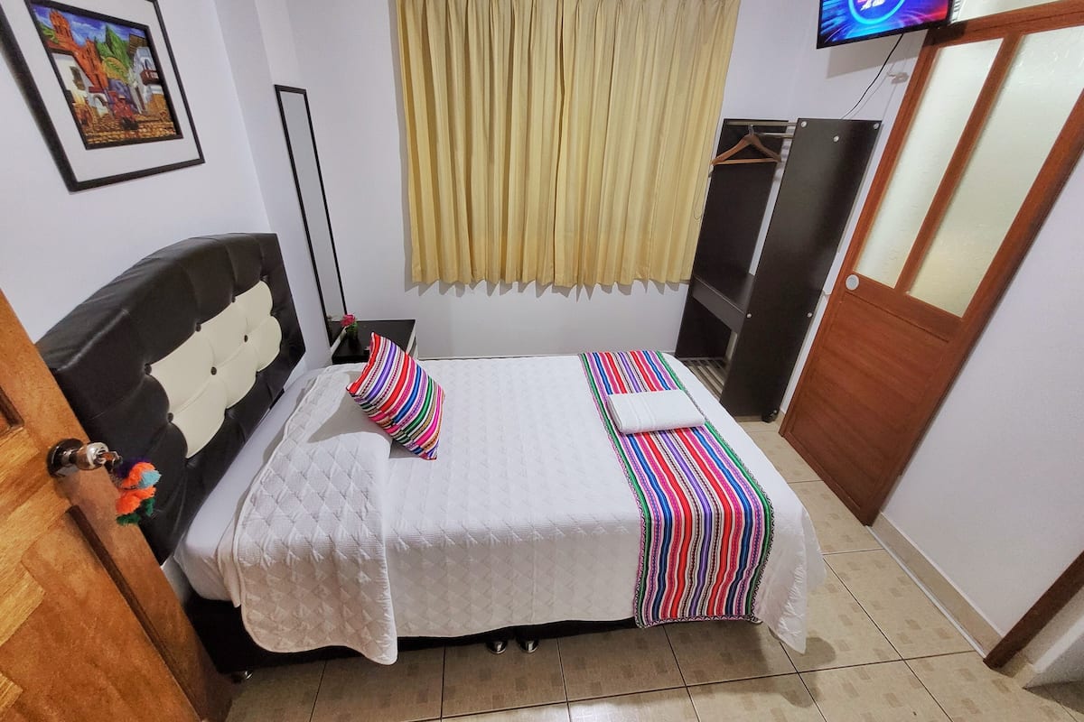 A bedroom with a bed, a TV, a wardrobe, and a painting on the wall.