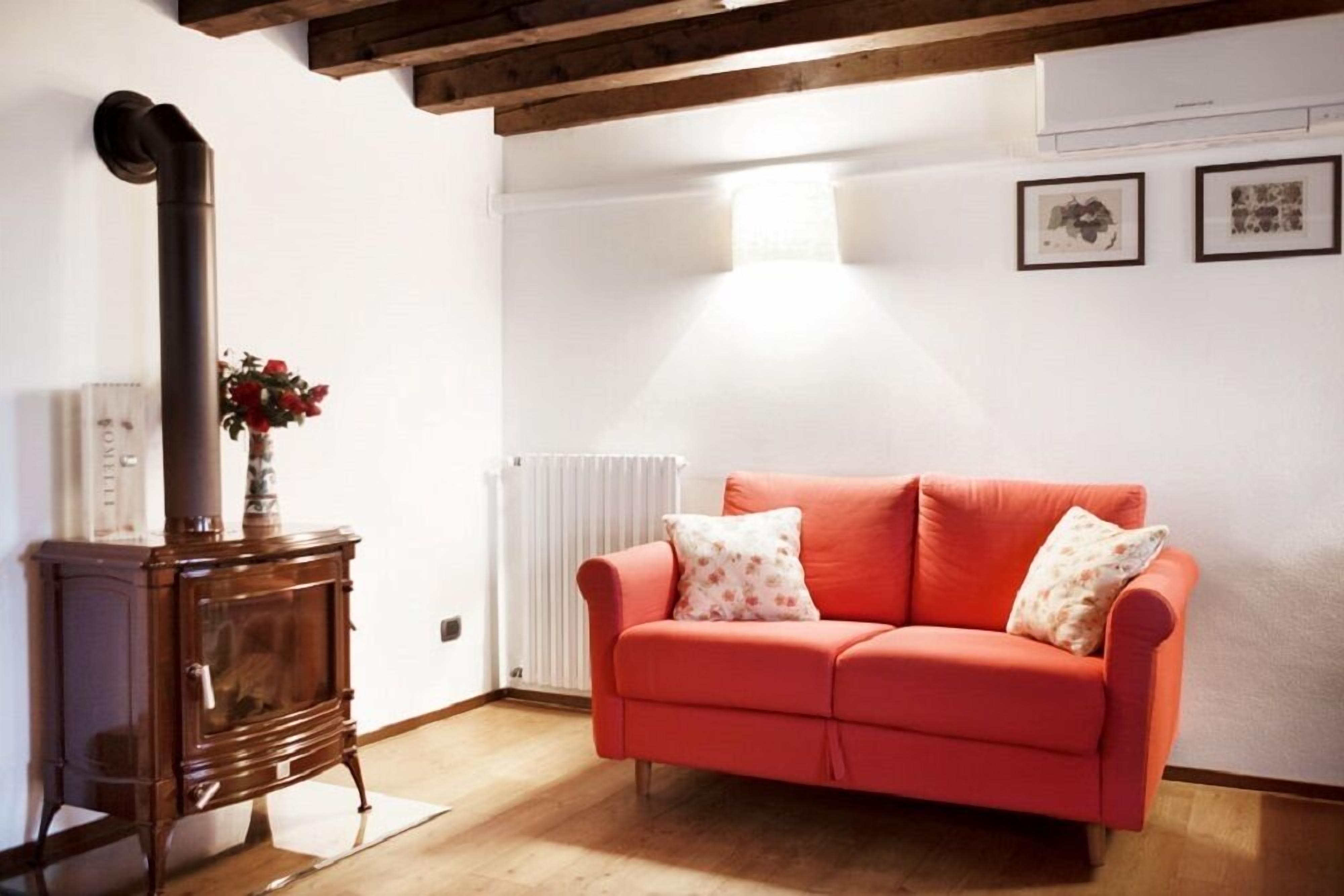 Ein gemütliches Wohnzimmer mit einem roten Sofa, einem Holzofen und einer Heizung.
