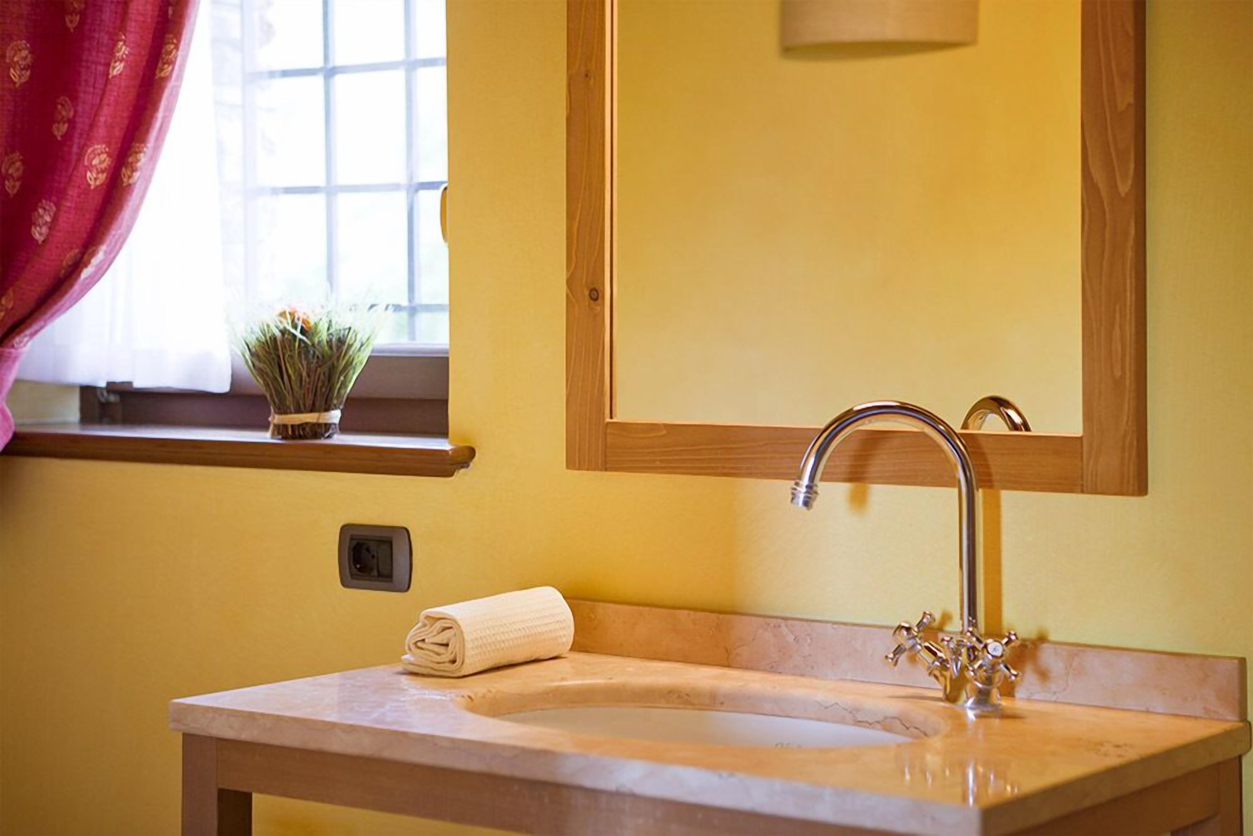 Un baño con lavamanos, espejo y ventana con cortinas.