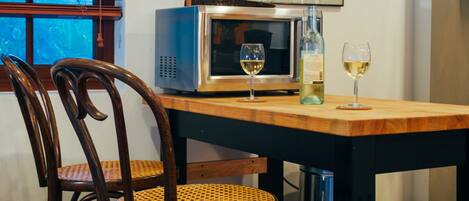 Un coin repas avec une table en bois, deux chaises, un four à micro-ondes, une bouteille et deux verres à vin.