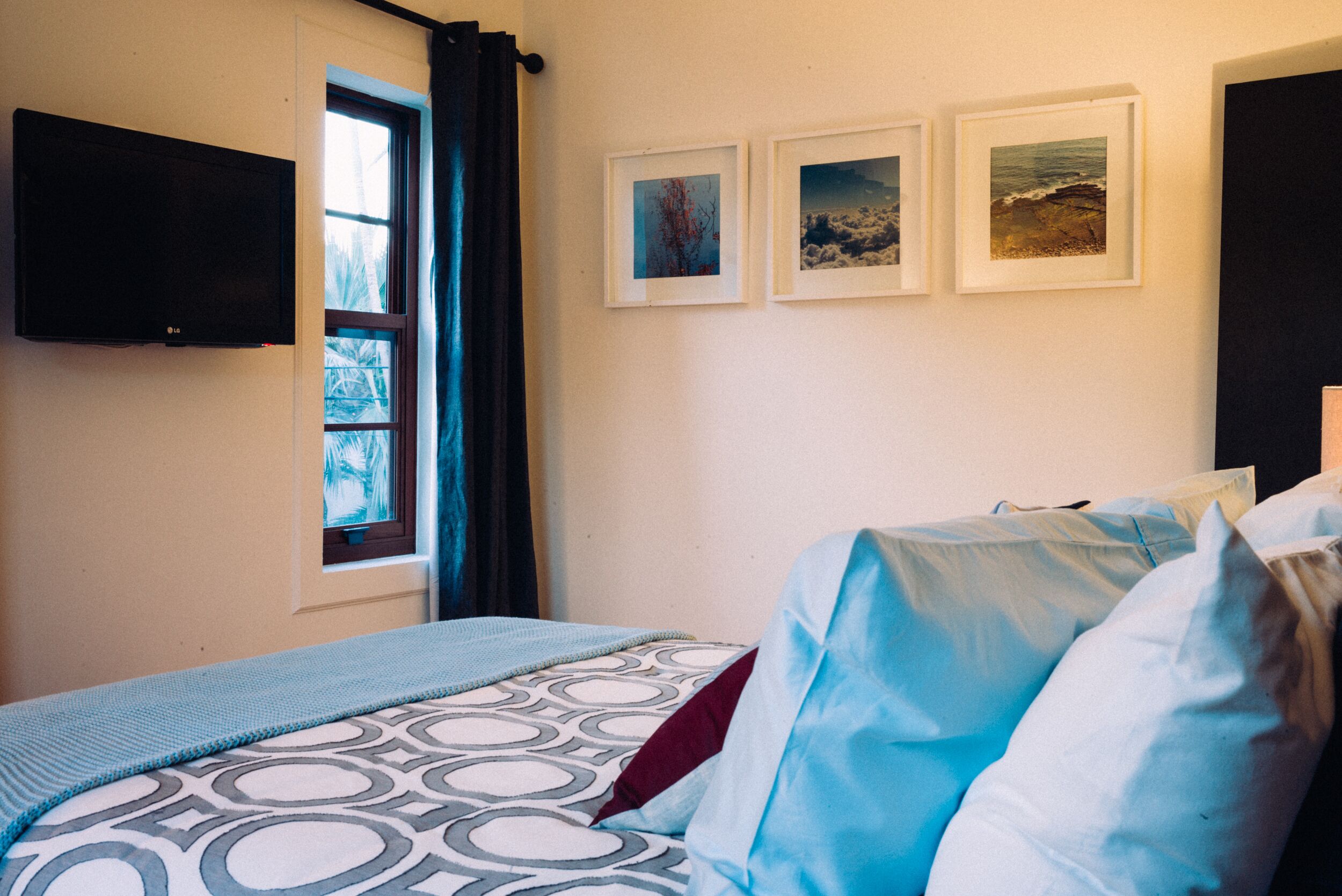 Une chambre à coucher avec un lit, un téléviseur fixé au mur et trois tableaux encadrés accrochés au mur.
