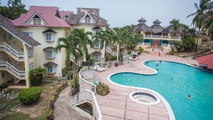 Een resort met een zwembad, palmbomen en een gebouw met een rood dak.