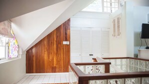 A room with wooden flooring, white walls, a wooden sloped ceiling, a white door with shutters, and a glass railing.