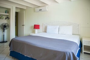 A bedroom with a bed, a bedside table with a lamp, a fan, and an air conditioning unit.