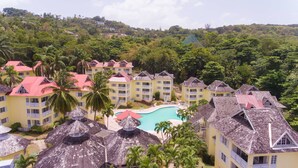 A resort with multiple yellow buildings, a central swimming pool, and surrounding lush greenery.