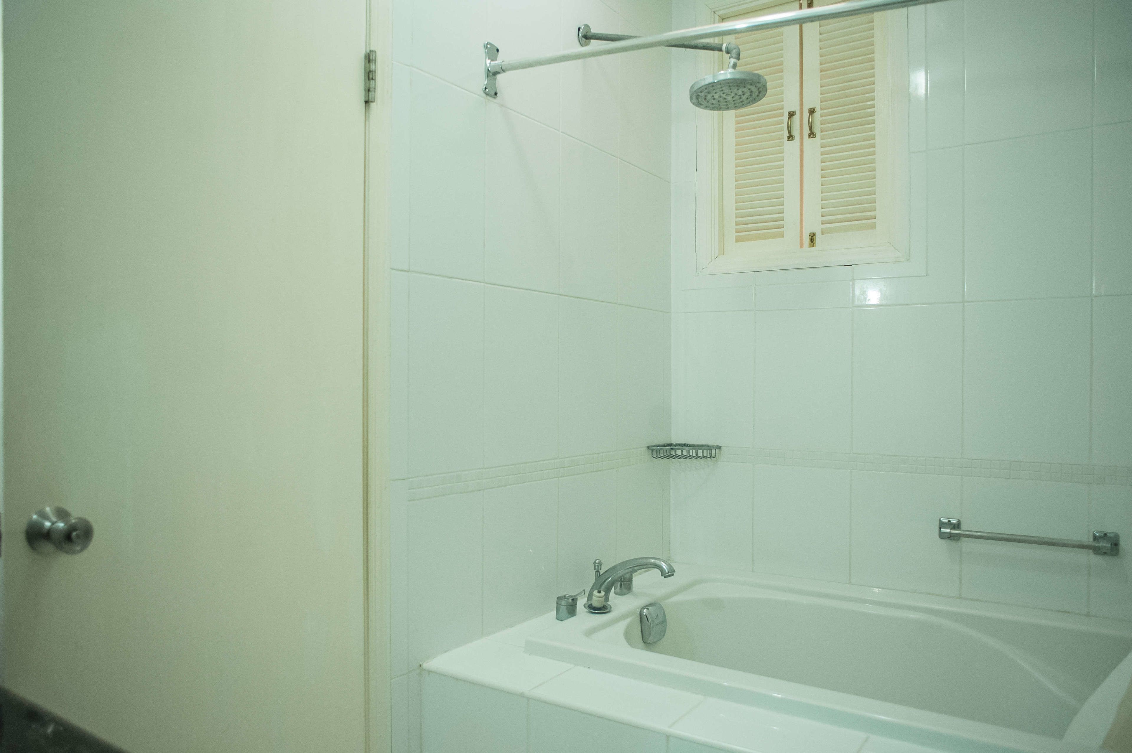 A bathroom with a bathtub, a showerhead, and a window with shutters.