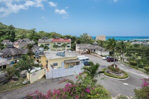 A coastal resort with thatched-roof buildings, a parking area, and a view of the ocean.