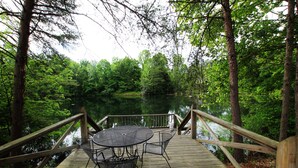 A wooden deck with a table and chairs overlooking a lake, surrounded by trees.