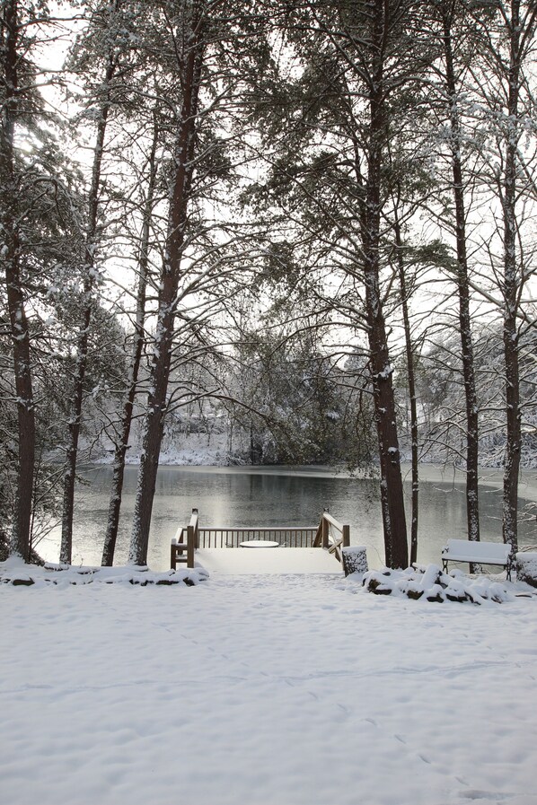 Un parque cubierto de nieve con un banco de madera y una barandilla con vistas a un lago.
