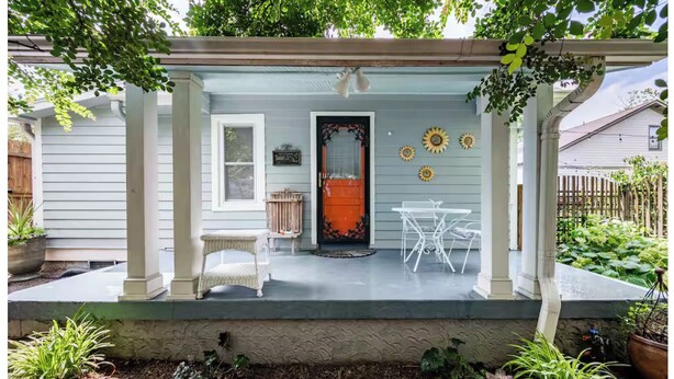 A covered porch with a table and chairs, a door, and decorative sunflowers. - PEACEFUL PRIVATE COTTAGE-WALK TO PARK-5 MINS TO DOWN TOWN (Nashville)