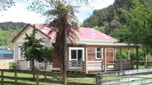 A wooden cabin with a red roof, a porch, and a fenced yard.