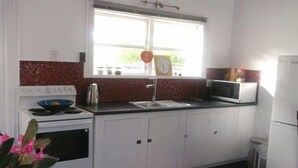 A kitchen with white cabinets, a stove, a microwave, and a red rug.