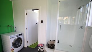 A compact bathroom with a washing machine, a small stool with a Union Jack flag, and a glass-enclosed shower area.
