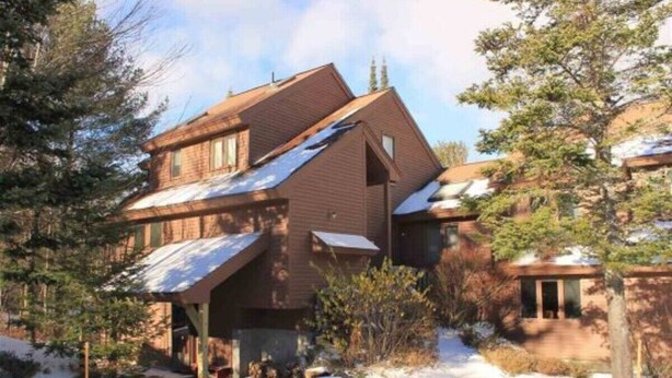 Una casa de dos pisos con techo inclinado, rodeada de árboles y nieve.