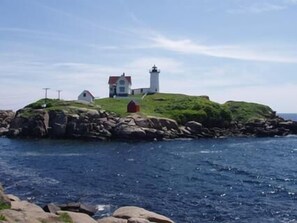 A lighthouse on a grassy island with a small building nearby, surrounded by water.