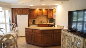 A kitchen with wooden cabinets, a granite countertop, a built-in microwave, and a TV on a cabinet. - Tilghman Lakes By the Sea (North Myrtle Beach)