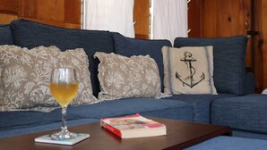 Un canapé bleu avec des coussins à motifs, un verre de vin blanc et un livre sur une table en bois.