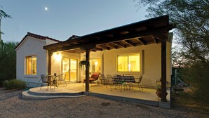 A house with a covered patio, a dining area with chairs and a table, and a large window.