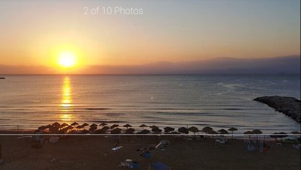 A beach with the sun setting over the water, a rocky breakwater, and beach chairs and umbrellas. - La Perle Bleue (Le Kram)
