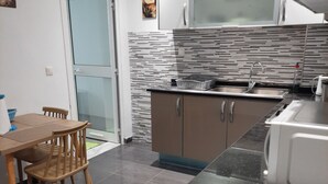 A modern kitchen with a dining area, featuring a tiled floor, a microwave, a sink, and a cabinet. - La Perle Bleue (Le Kram)