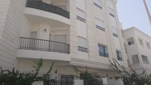 A multi-story residential building with balconies, a gated entrance, and a street lamp. - La Perle Bleue (Le Kram)