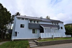 Ein modernes, zweistöckiges Haus mit geneigtem Dach, großen Fenstern und einer Veranda.