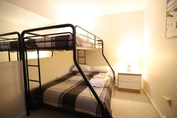 Ein Stockbett mit Kopfteil, ein Nachttisch mit Lampe und eine kleine Kommode.