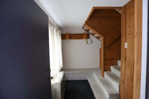 Eine Treppe mit Holzbodenstufen, die zu einer Zwischenebene, einer Tür und einem mit Vorhängen drapierten Fenster führt.