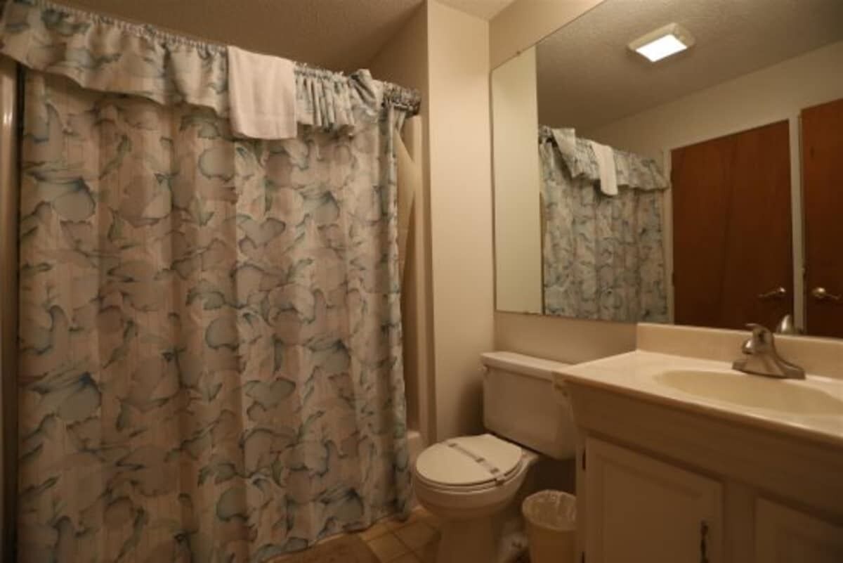 A bathroom with a toilet, sink, mirror, and shower curtain.
