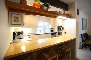 Une cuisine avec un bar en bois, des meubles blancs, une fenêtre et un coin repas avec des chaises.