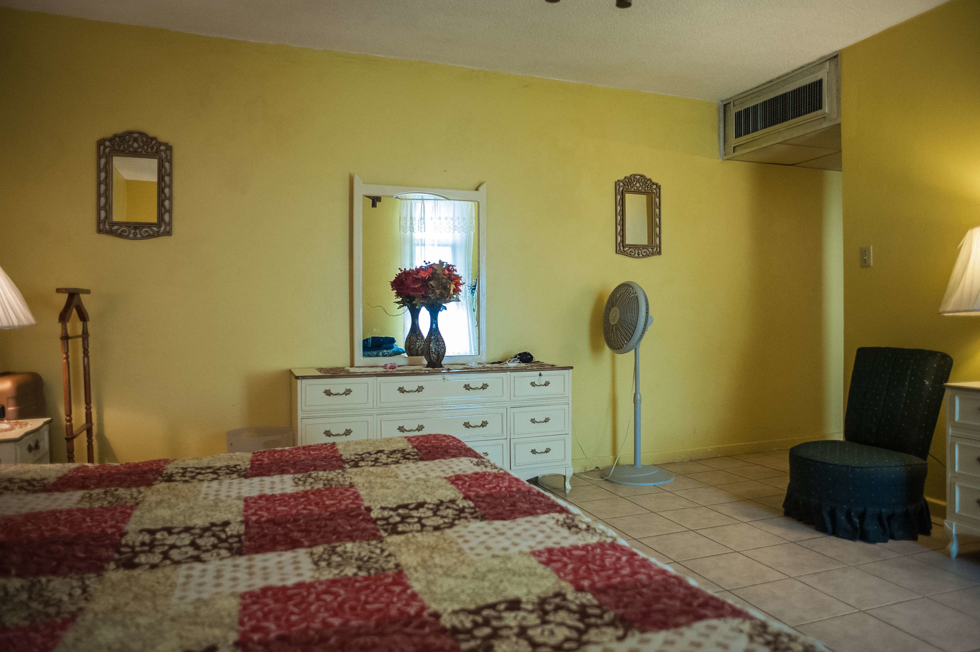 Une chambre à coucher avec un lit, une commode, un miroir et un ventilateur.