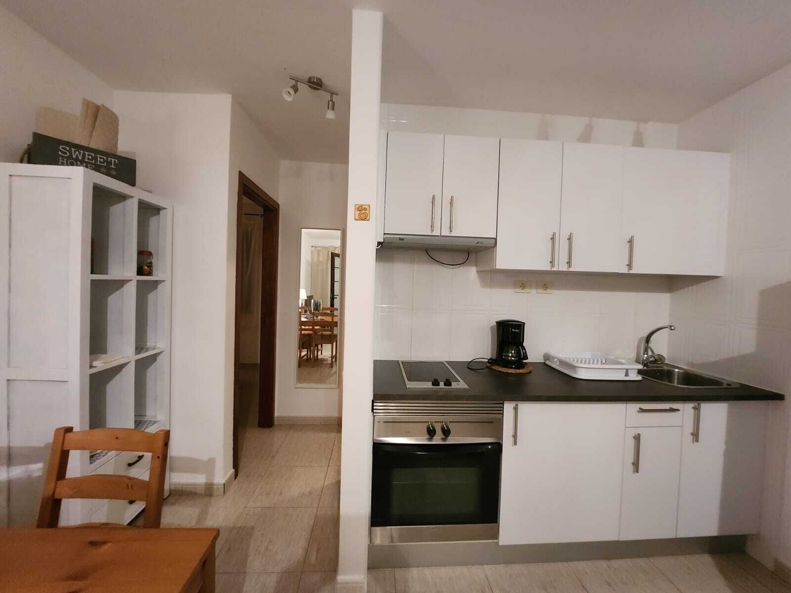 Cocina compacta con armarios blancos, encimera negra, cafetera y lavabo.