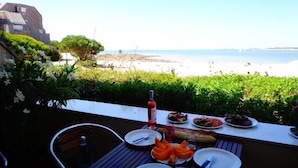 Un área de comedor al aire libre con vista a la playa, una botella de vino y diversos platos.