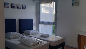 Una habitación con dos camas, una ventana y vistas, y una puerta.