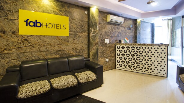 Uma área de recepção com um sofá de couro preto, uma placa amarela com a inscrição "fabHOTELS" e um painel decorativo.