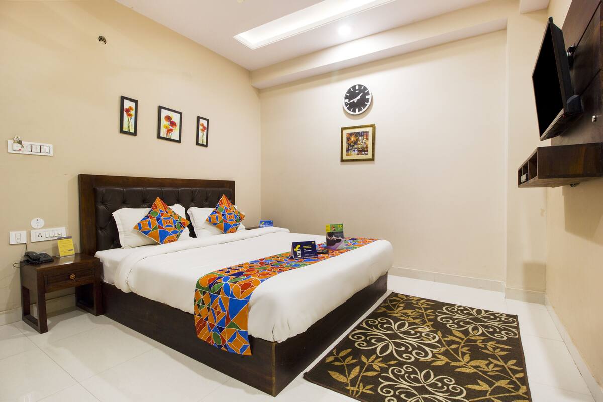 Uma cama bem arrumada com um cobertor colorido, uma mesa de cabeceira com um telefone e um relógio na parede.