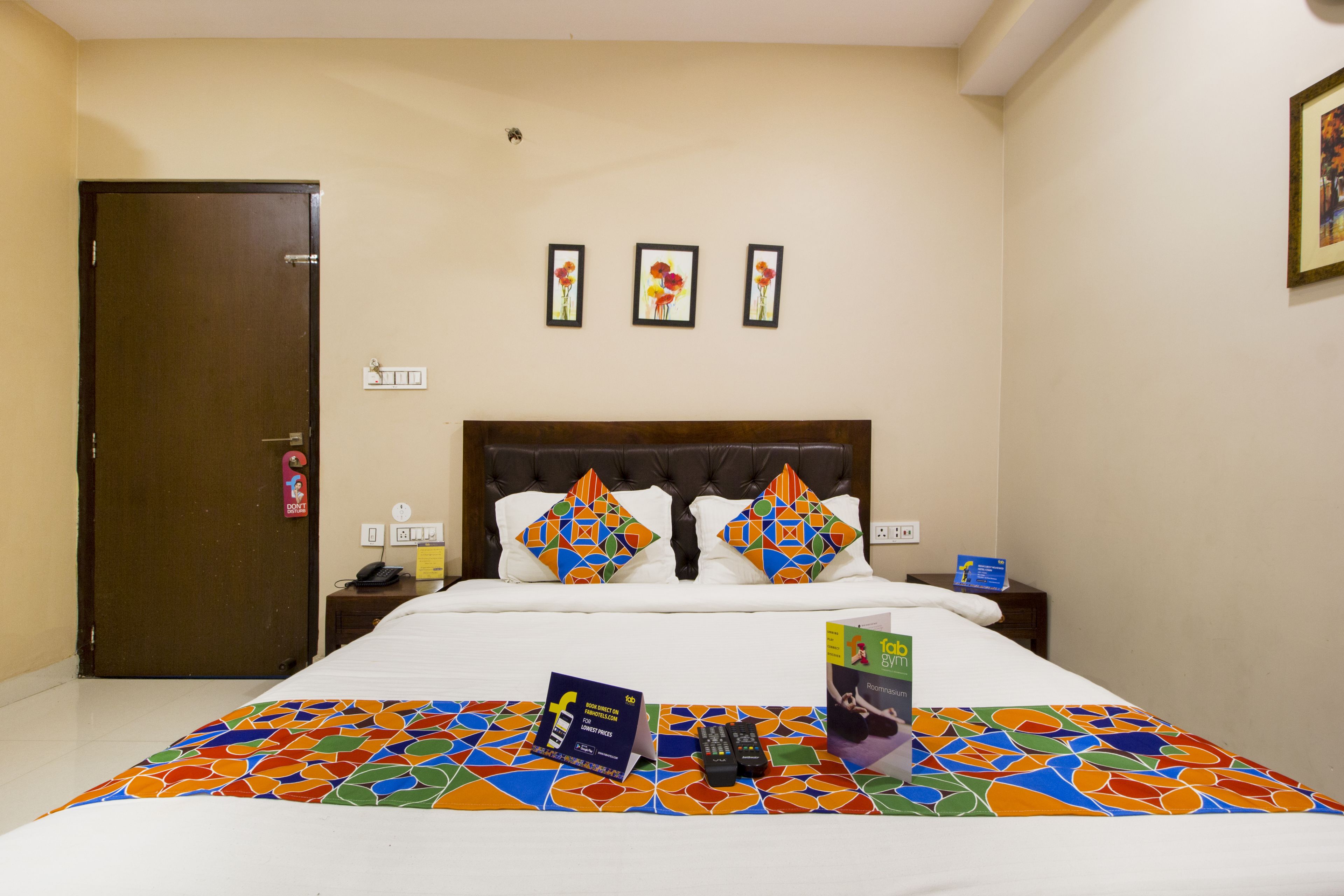 A hotel room with a bed, a nightstand, a door, and three framed pictures on the wall.