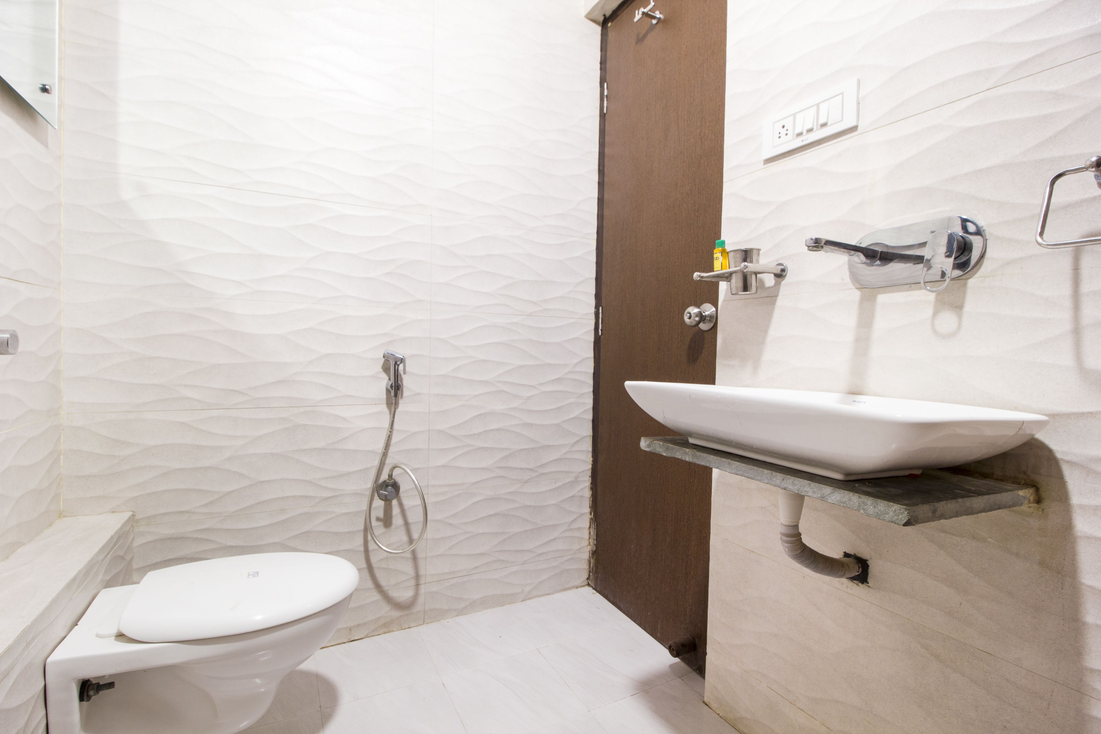 A bathroom with a toilet, a sink on an elevated shelf, a shower, and a door.