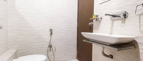 A bathroom with a toilet, a sink on an elevated shelf, a shower, and a door.