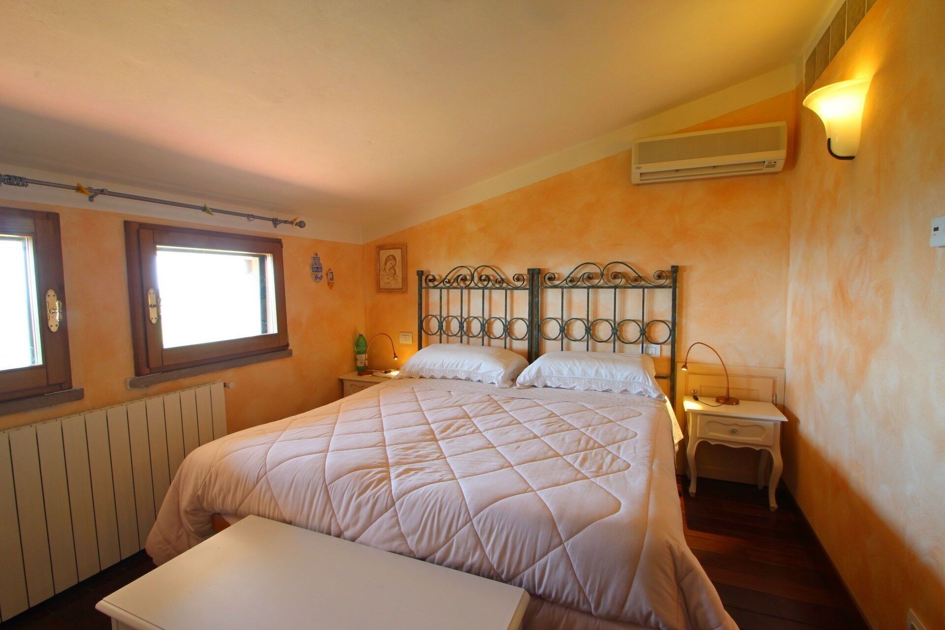 Une chambre à coucher comprenant un lit, des tables de chevet, une fenêtre, un climatiseur et un radiateur.