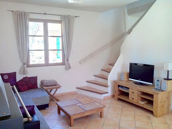 A compact living space with a sofa, a small table, a TV, and a staircase. - Lovely house in the Luberon with a pool in a charming location. (La Bastide-Des-Jourdans)