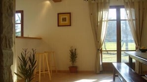 A room with a large window, a wooden bench, a small table, and two potted plants.