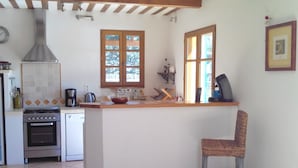 A kitchen with a central island, a stove, oven, and a sink. There is a chair and a window with a view of trees.
