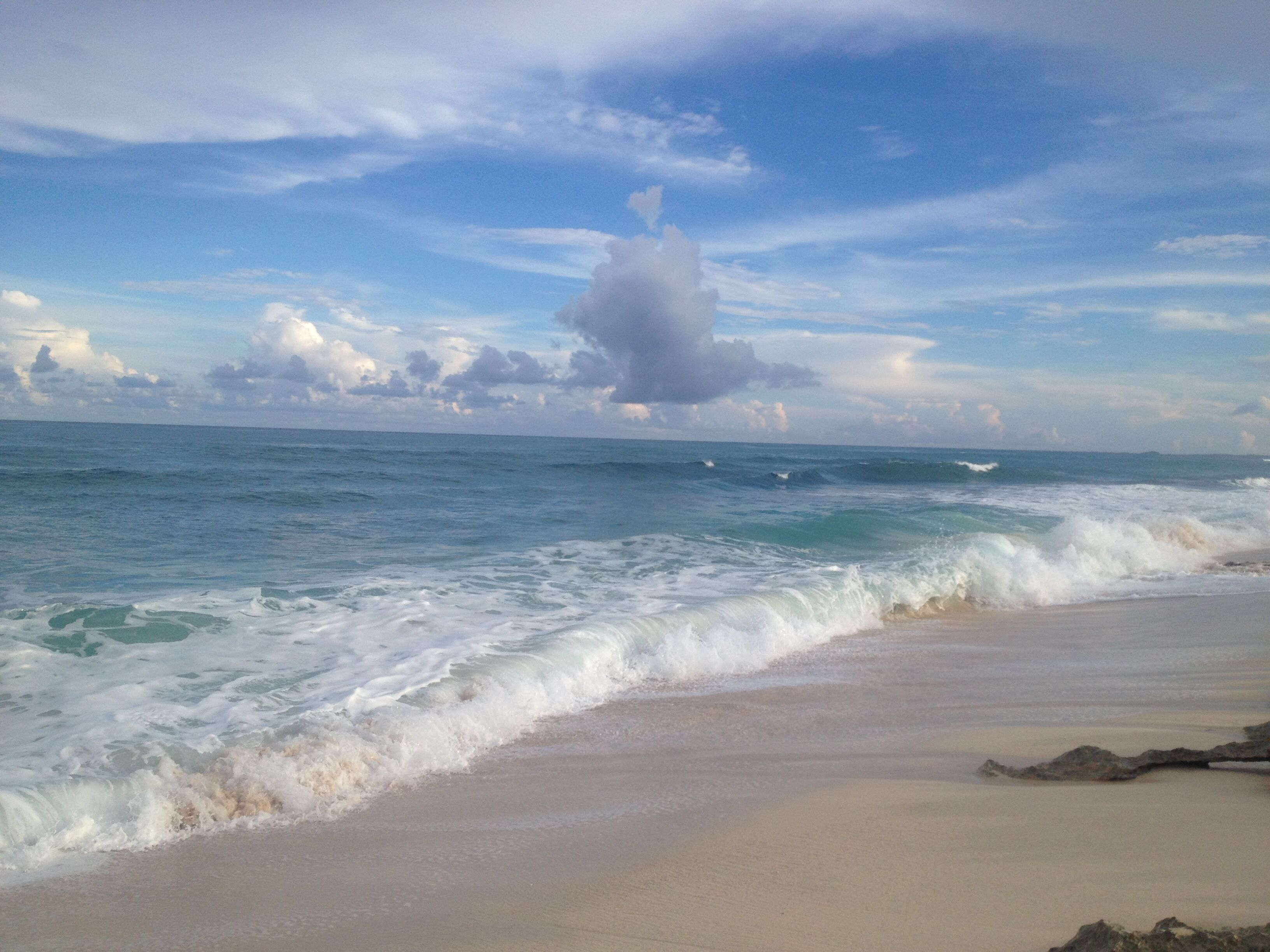 A beach with waves, a clear sky, and distant clouds.