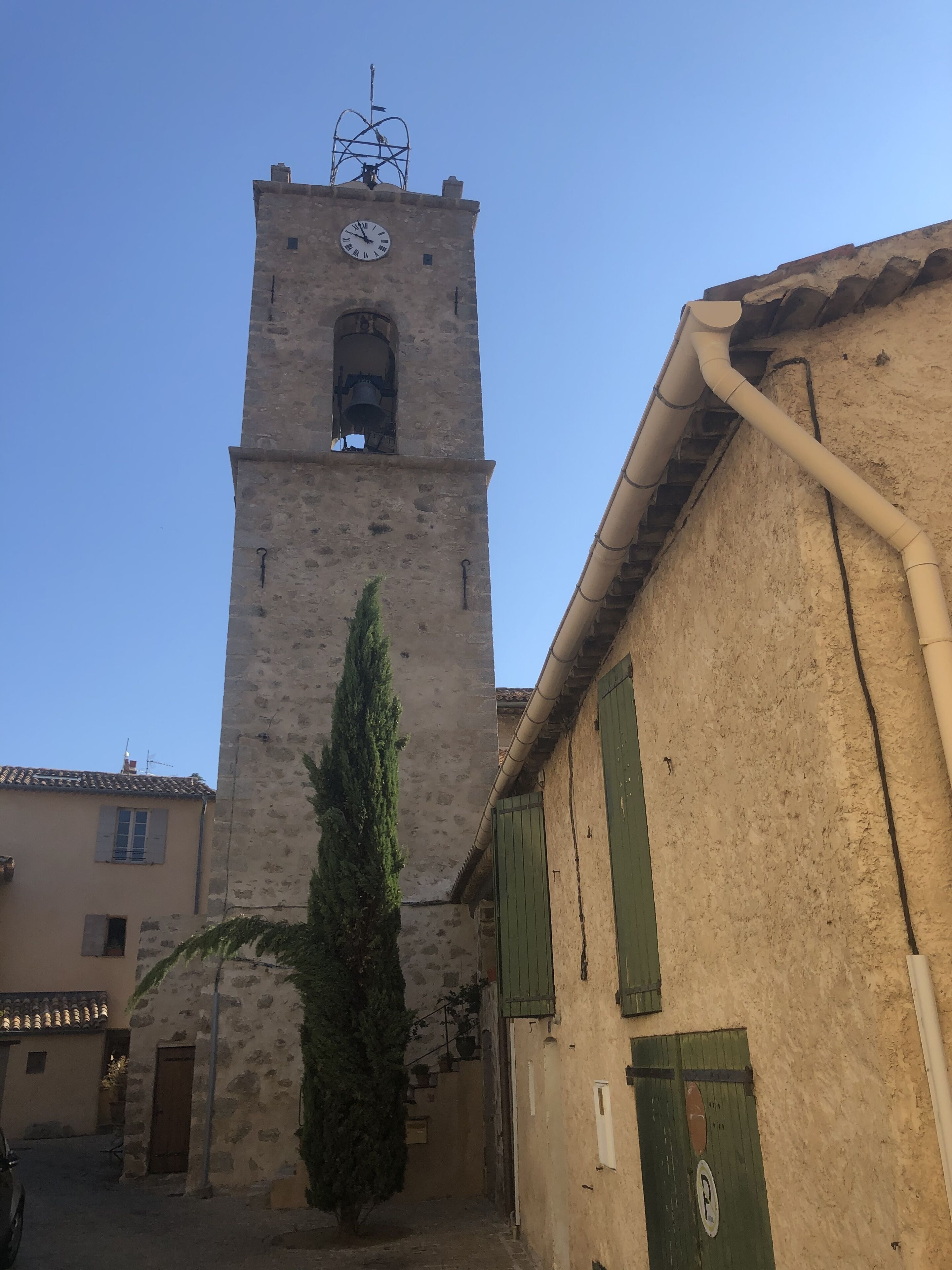 A historic tower with a clock, a tall cypress tree, and traditional architecture.