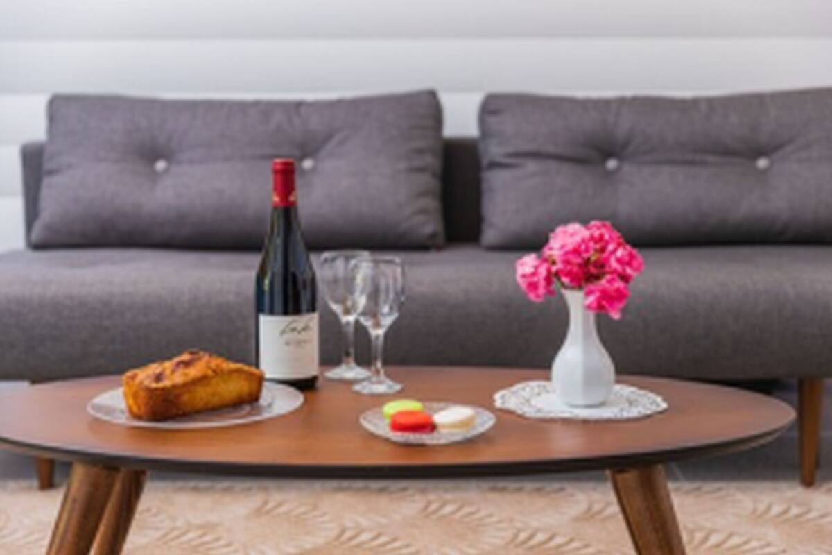 Een ronde houten tafel met een fles wijn, twee glazen, een brood en een klein bord met kleurrijke macarons.