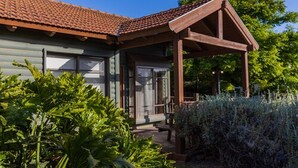 Een houten huis met een pannendak en een overdekte veranda, met weelderige begroeiing op de voorgrond.