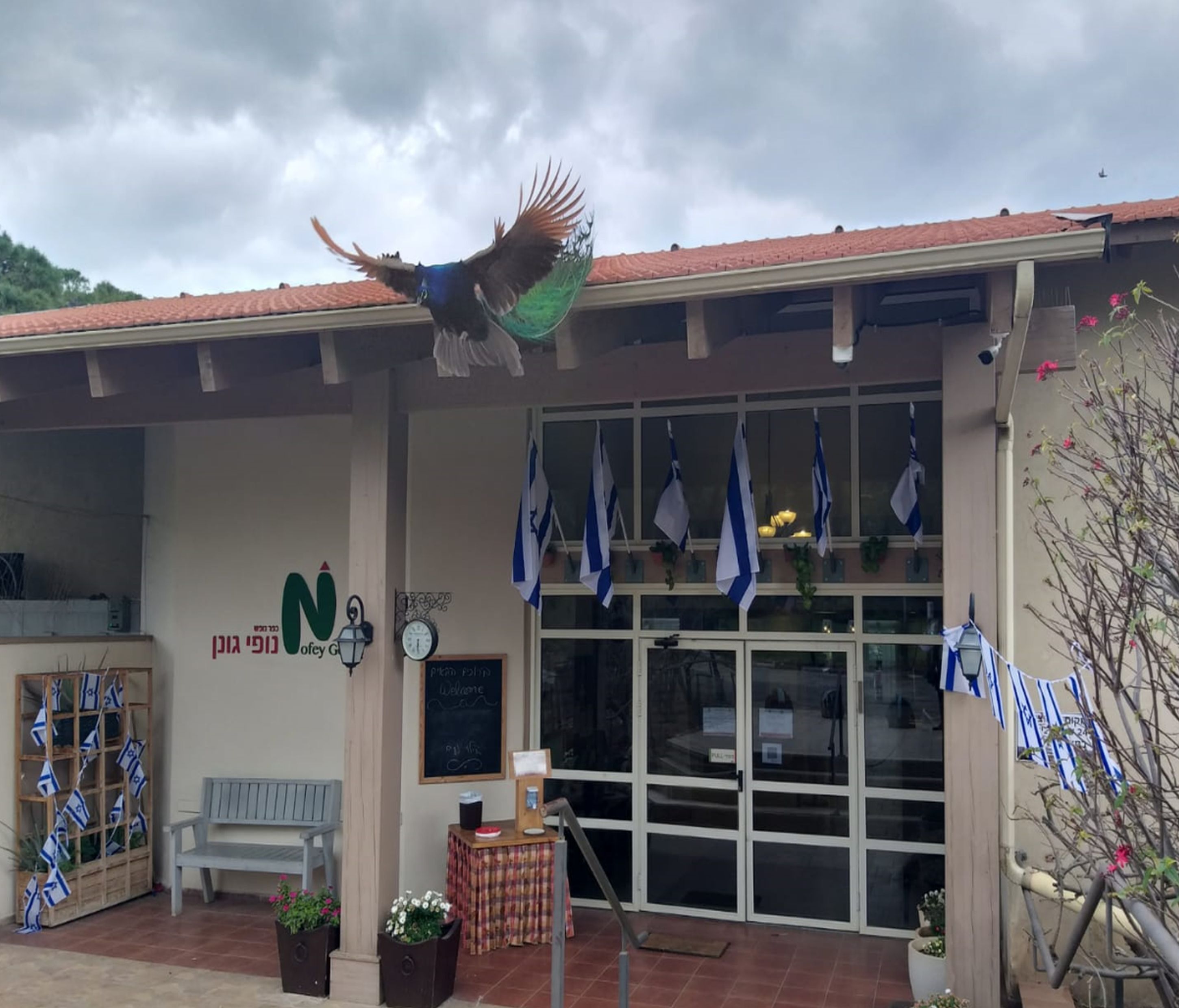 A building with a tiled roof, a bench, a clock, flags, and a welcome sign.