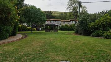 A grassy backyard with a gazebo, a pathway, and a row of houses in the background.